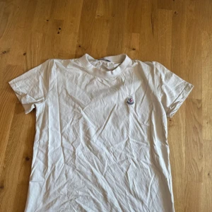 Vit Moncler t-shirt med logga -  t-shirt från Moncler i mjuk bomull med klassisk rund hals och korta ärmar. På bröstet sitter Monclers ikoniska broderade logga i blått och rött. Enkel och clean design som funkar till allt. Perfekt för dig som gillar stilrena märkesplagg. Nästan helt oanvänd! Prislapp kommer med.