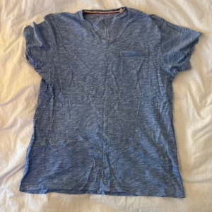 Blå v-ringad t-shirt från Esprit - Snygg blå t-shirt från Esprit med v-ringning och bröstficka. T-shirten har ett melerat mönster och är gjord i mjuk bomull. Perfekt för chill dagar och enkel att matcha med jeans eller shorts.