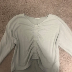 Ljusgrön croppad tröja  - Snygg ljusgrön långärmad tröja med v-ringad hals och croppad passform. Framsidan har en cool rynkad detalj som ger extra stilpoäng. Perfekt för dig som gillar en chill och trendig look.