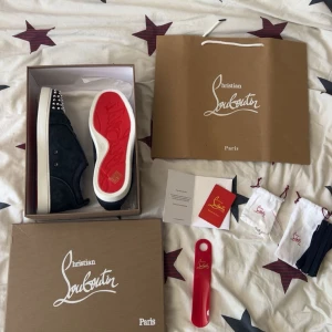 Christian Louboutin sneakers med spikar - Säljer ett par mörkblå sneakers från Christian Louboutin i mocka med vita sulor och ikonisk röd undersida. Skorna har snörning och är dekorerade med silverfärgade nitar på tån för en edgy vibe. Kommer med originalkartong, dustbags och skohorn.