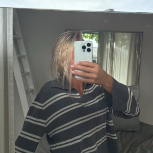 Grå långärmad pikétröja med vita ränder från WARE - Säljer en grå långärmad pikétröja från WARE med vita horisontella ränder. Tröjan har en klassisk krage och v-ringning, perfekt för en avslappnad men stilren look.