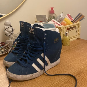 Turkosa klackar från adidas - Snygga blå high top sneakers från Adidas med klassiska vita ränder och vit insida. Supercoola men tyvärr för små för mig. Smutsig sula men det går att tvätta bort har bara inte orkat.