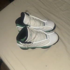 Nike Air Jordan 13 Retro vit/grön - Nike Air Jordan 13 Retro sneakers i vitt och grönt med svarta detaljer. Ovandel i skinn och mocka, klassisk snörning och rund tå. Sulan har unika gröna hologramdetaljer och mönstrad undersida. Perfekta för dig som gillar streetwear och basketstil.