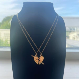 Guldiga best friends-halsband hjärta - Två matchande guldiga halsband med varsin halva av ett brustet hjärta, perfekt för dig och din bästa vän. Hängena har en stilren design och kedjorna är tunna och eleganta. Säljs som ett set om två delar. Rostfri kjedjan är 40 cm lång 