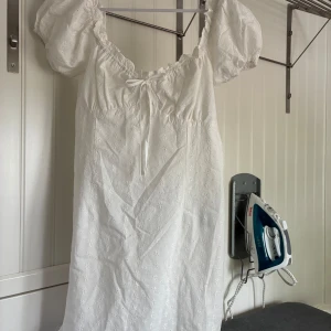 Vit blommig kortklänning med puffärm - Superfin vit kortklänning med broderade blommor och puffärmar. Klänningen har en söt rosett framtill, v-ringning och är tillverkad i ett lätt bomullstyg. Perfekt för sommarens alla tillfällen! Endast provad med prislappen kvar! Säljes endast då den är förliten för mig, storlek 44 men skulle säga att den är mer som en 38/M🥰