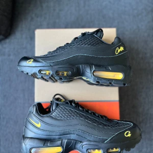 Nike Air Max 95 X Corteiz - Säljer ett par Nike Air Max 95 i svart med gula detaljer. Skorna har synliga Air Max-enheter i sulan, broderade gula loggor och snörning. Ovandelen är i syntet och skinn med flera lager och rund tå. Perfekta för dig som gillar streetwear.