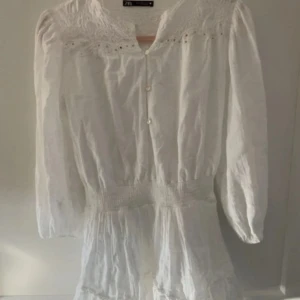 Vit klänning med spetsdetaljer från Zara - Säljer en romantisk vit klänning från Zara i storlek XS. Klänningen har vackra spetsdetaljer upptill, knappar framtill och långa ärmar. Perfekt för sommarens tillfällen eller studentfirande.