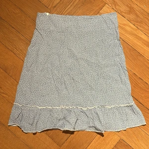 Blå blommig kjol från Brandy Melville - Supersöt blå kjol med vitt blommönster från Brandy Melville. Kjolen har volang nertill och är perfekt att styla med en enkel topp eller stickad tröja🩷🫶🏻🤩