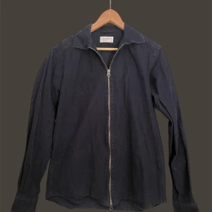 John Henric overshirt  - Säljer en mörkblå skjorta från John Henric i Manchester material med hel dragkedja framtill. Skjortan har klassisk krage och långa ärmar, perfekt för en stilren och avslappnad look. Passar lika bra till jeans som till chinos.