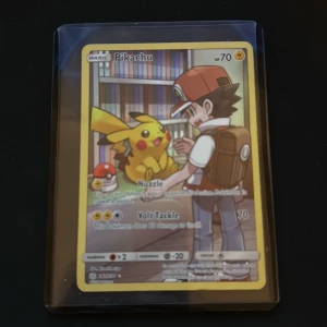 Pikachu (Pokémonkort 241/236) - Samlarkort med Pikachu och Ash framför en bokhylla. Kortet har attacker som Nuzzle och Volt Tackle. Perfekt för Pokémon-fans och samlare som gillar unika och färgglada kort. Kortet är illustrerat av Hitoshi Ariga och har nummer 241/236.