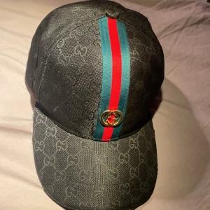 Keps - En svart keps med gröna och röda render men en guld loga i mitten