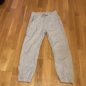 Grå mjukisbyxor med dragsko - Grå mjukisbyxor med resår i midjan och benslut samt justerbar dragsko framtill. Byxorna har en avslappnad passform och är tillverkade i mjukt bomullsmaterial. Perfekta för en chill dag hemma eller när du vill vara extra bekväm.