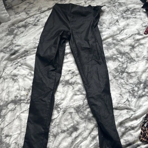 Svarta leggings från Pieces - Säljer ett par svarta leggings från Pieces i storlek L. Byxorna har en tight passform och är gjorda i ett syntetmaterial med dragkedja i sidan för enkel påtagning. Perfekta till en snygg och enkel outfit.