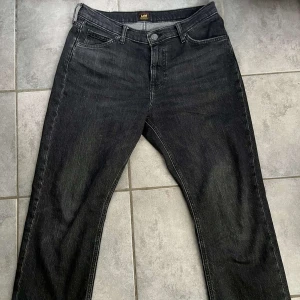 Svarta jeans från Lee - Säljer ett par svarta jeans från Lee med klassisk femficksdesign och raka ben. Jeansen har normal passform och stängs med dragkedja och knapp. Perfekta för dig som gillar en enkel och stilren look. Storleken är 32/32 