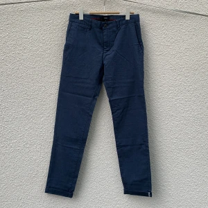 Mörkblå chinos från Jules - Säljer ett par mörkblå chinos från Jules i slim fit-modell. Byxorna har klassiska fickor fram och bak, bälteshällor och stängs med knapp och dragkedja. Materialet är mjukt och stretchigt med bomull och elastan.