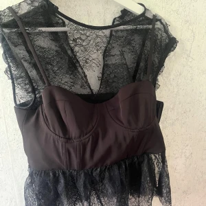Svart spetsblus med korsett från Zara - Säljer en svart blus från Zara med transparent spets och inbyggd korsett. Blusen har smala axelband och vacker spetsdetalj över hela plagget. Perfekt för dig som vill ha en edgy och trendig look.