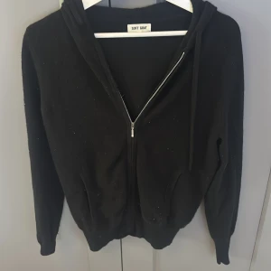 Svart hoodie med dragkedja från Soft Goat - Mysig svart hoodie från Soft Goat i mjukt material. Tröjan har dragkedja framtill, huva med snören och långa ärmar. Perfekt för en avslappnad stil.