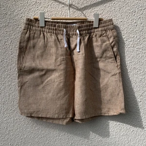 Beiga linneshorts från Weekday - Beiga shorts från Weekday i 100% linne med elastisk midja och vit snörning. Två sidofickor fram och en backficka. Storlek M.