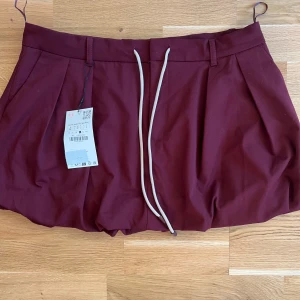 Vinröd kjol Zara  - Säljer en vinröd kortkjol med dragsko i midjan med en puffig design. Kjolen har två fickor fram och låtsats fickor bak. Storlek l men passar s-m också då man kan knyta den i midjan. Aldrig använd 😊