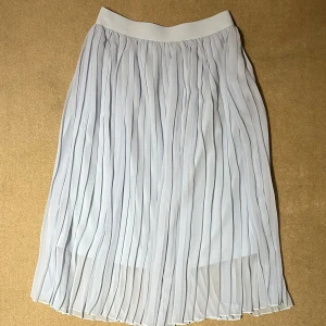 Ljusblå plisserad kjol - NAKD - Säljer en ljusblå plisserad kjol med resår i midjan. Kjolen är vadlång och har ett luftigt, skirt tyg som ger ett snyggt fall. Perfekt för dig som gillar en stilren och enkel look.