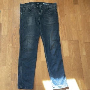 Mörkblå Replay jeansbyxor - Säljer ett par stensvarta jeans från Replay med klassisk femficksdesign och raka ben. Jeansen har subtila slitningar och tydliga sömmar, perfekt för en avslappnad stil. Passar dig som gillar tidlös denim.