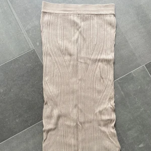 Beige ribbad långkjol - Säljer en beige ribbad långkjol med hög midja. Kjolen har en rak passform och är tillverkad i ett stretchigt material som sitter bekvämt. Perfekt att styla med en enkel topp eller stickad tröja.