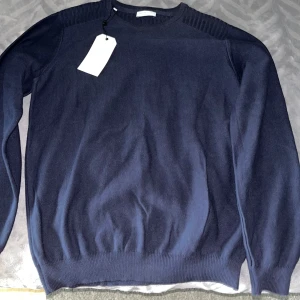 Mörkblå stickad tröja från Selected Homme - Snygg mörkblå stickad tröja från Selected Homme med rund halsringning och ribbade detaljer vid axlar, ärmslut och nederkant. Perfekt för lager-på-lager och passar till många olika stilar.