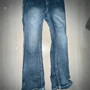 Blå bootcut jeans med broderad bakficka - Säljer ett par blå bootcut jeans med snyggt vitt broderi på bakfickan. Jeansen har klassisk femficksdesign och markerade sömmar. Perfekta för dig som gillar en lite utsvängd stil och detaljer på fickorna.