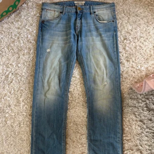 Ljusblå jeansbyxor från Maison Scotch - Säljer ett par ljusblå jeans från Maison Scotch med klassisk femficksdesign och lätt slitna detaljer på låren. Jeansen har raka ben och normal passform. Perfekta till vardags för en avslappnad stil.