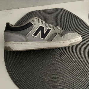 Grå New Balance sneakers - Säljer ett par snygga grå New Balance sneakers med svart och vitt N-logga på sidan. platt sula. och funkar året runt. Köpt för 2000 säljer för 599kr