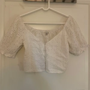 Vit broderad blus från NLY Trend - Superfin vit blus från NLY Trend med broderade blommor och korta puffärmar. Toppen är croppad, har knappar framtill och elastisk offshoulder-ringning. Perfekt för varma dagar och möjligtvis på skolavslutning eller liknande 💖storlek 36/S. Använt fåtal gånger men finns inga syndliga tecken på användning 💖