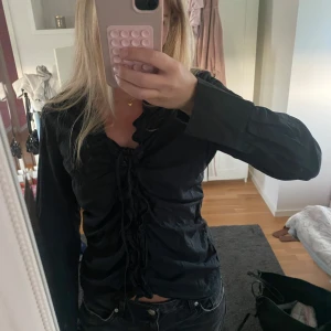 Svart skjorta med snörning - Säljer en svart skjorta med lång ärm och snygg snörningsdetalj framtill. Skjortan har krage. Köpt på en vintage butik. 