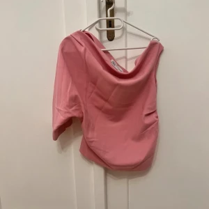 Rosa oneshoulder topp från Zara - Trendig rosa topp från Zara med oneshoulder-design. Toppen har en asymmetrisk skärning och är tillverkad i ett mjukt, slätt material. Perfekt för dig som vill sticka ut med en unik och stilren look.