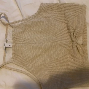 Beige glittrig croppad linnetopp från ONLY - Säljer en beige glittrig croppad linnetopp från ONLY. Toppen har smala axelband och ett diskret knyt fram. Perfekt för dig som vill ha något extra till sommaren💗