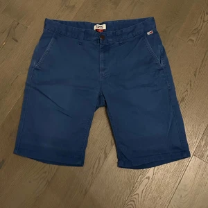 Blå shorts från Tommy Hilfiger - Snygga blå shorts från Tommy Hilfiger med klassisk passform. Shortsen har sidofickor, bakfickor med knappar och en liten logga ovanför ena bakfickan. Perfekta för varma dagar. 