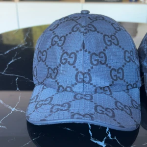  keps från Gucci med GG-mönster - Säljer en keps från Gucci med det klassiska GG-mönstret över hela kepsen. Kepsen har böjd skärm och justerbar rem baktill. Materialet är polyester och kepsen har en modern, stilren look.