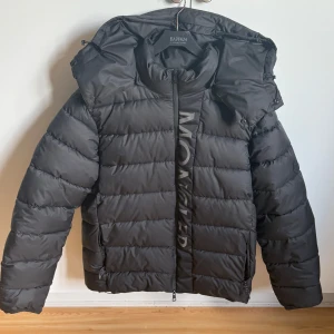 Svart pufferjacka från Moncler - Säljer en svart pufferjacka från Moncler med huva och dragkedja framtill. Jackan har en klassisk quiltad design. Perfekt för kyliga dagar.