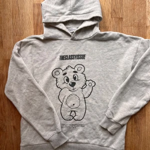 Grå hoodie med björntryck  - Säljer en ljusgrå hoodie med stor söt björn på framsidan och tryck på ärmen. Tröjan har huva och ribbade muddar. Perfekt för en avslappnad stil och streetwear-vibe. Storleken säger XS, men enligt mig är det mer M/L då den är oversized! Mycket skön, och lite ”tyngre” i materialet 