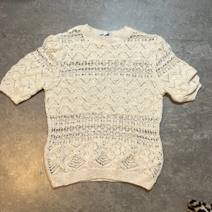 Vit stickad tröja från Zara - Säljer en vit stickad tröja från Zara med korta ärmar och ett snyggt hålmönster. Tröjan har rund halsringning och ett unikt strukturmönster över hela plagget. Perfekt för lager-på-lager och passar till många olika stilar.