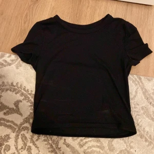 Svart croppad t-shirt från H&M - En enkel svart croppad t-shirt från H&M med rund halsringning och korta ärmar. Perfekt att matcha med jeans eller kjol för en stilren look. Aldrig andvänd