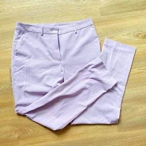 Ljuslila kostymbyxor från KappAhl - Snygga ljuslila kostymbyxor från KappAhl med raka ben och pressveck. Byxorna har hällor för bälte, dold dragkedja och hyska fram samt två fuskfickor bak. Perfekta för en stilren look.