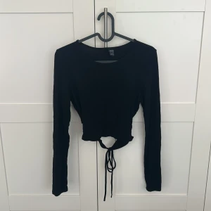 Svart croppad långärmad topp med knut  - Säljer en svart croppad långärmad topp med knyt baktill. Perfekt till jeans eller kjol för en trendig look. Enkel och stilren design som passar till många outfits.