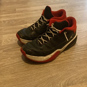 Svarta och röda Jordan 3 aura sneakers - Säljer ett par svarta Jordan 3 aura sneakers med röda och vita detaljer. Skorna har snörning, rund tå och en platt sula. Insidan är röd och yttersulan har en tydlig Jumpman-logga. Perfekta för dig som gillar streetwear och basketstil.