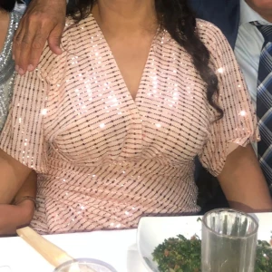 Glittrig ljusrosa kortklänning - Superfin ljusrosa kortklänning med glittriga paljetter och v-ringning. Klänningen har korta ärmar och ett snyggt omlottliknande fall över bysten. Perfekt för dig som vill sticka ut med lite extra bling!