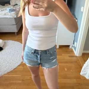 Blå jeansshorts från Zara, strl 34 - Snygga blå jeansshorts från Zara i storlek 34. Modellen är midwaist med klassisk femficksdesign, slitna detaljer och råa kanter nertill för en avslappnad vibe. Perfekta till sommaren och lätta att matcha med allt. Dragkedja och knapp framtill.