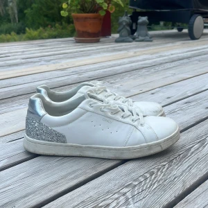 Vita sneakers från ONLY med glitter - Snygga vita sneakers från ONLY med silvriga detaljer och glittrig häl. Skorna har snörning. Och är i storlek 41. Jag säljer domhär för att dom är förstora men jag har använt dom några gånger, så de finns tecken på användning💕