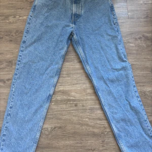 Blå mom jeans - Byxorna har en avslappnad passform och raka ben, perfekt för en chill och trendig look. Färgen är ljusblå denim 