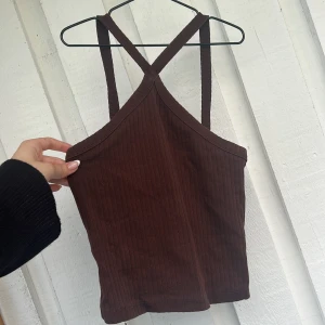 Brun ribbad linnetopp med korsade band - Säljer en brun ribbad linnetopp med smala axelband som korsas. Toppen är croppad och har en tight passform, perfekt till jeans eller kjol. Materialet är mjukt och stretchigt, vilket gör den superbekväm att bära.