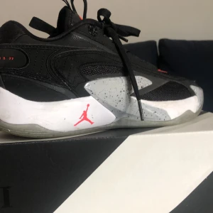Basket skor, Luka 2 strl 38.5 - Snygga svarta Nike Jordan, Luka 2 basketskor, med röda detaljer och vit/grå sula. Skorna har snörning, mesh och syntetpaneler samt den klassiska Jumpman-loggan på sidan. Perfekta för dig som gillar sportig och modern stil. Pris kan diskuteras😁😁