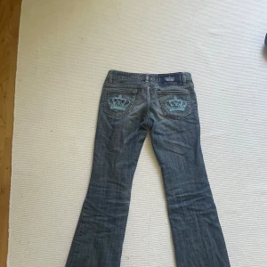 Victoria Beckham blå bootcut jeans - Snygga blå jeans från Victoria Beckham med bootcut passform. Bakfickorna har broderade ljusblå kronor som ger en unik och lyxig vibe. Klassisk femficksmodell i mjukt denimtyg med låg midja och diskret tvättad look.